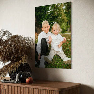 vertical wooden portrait of two brothers in matching white shirts displayed above wooden sideboard with dried pampas grass and black decorative vase in modern home setting