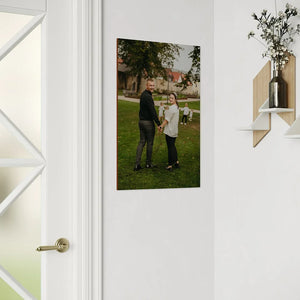 single vertical wooden family portrait displayed in bright hallway showing couple holding hands on grass with geometric wall shelf and decorative vase