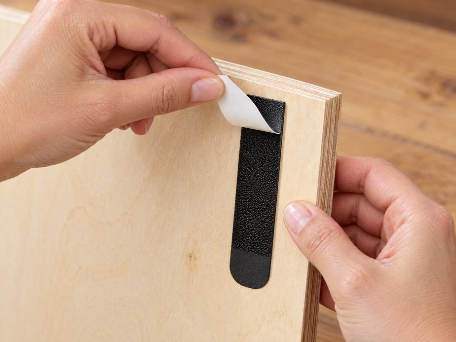 Schutzfolie wird von einem Klebestreifen auf der Rückseite des Holzposters abgezogen